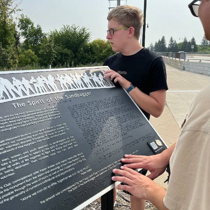 Ethan Thiseth, "viewing" the artwork embossed on one of the bronze plaques. He was thrilled that not only could he read about the art piece, he could feel the sculpture. Also pictured reading the braille on the plaque is Edward Freer of Langdon.